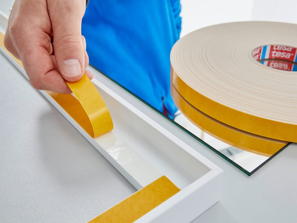 Double-sided foam tape being applied to mount a mirror.